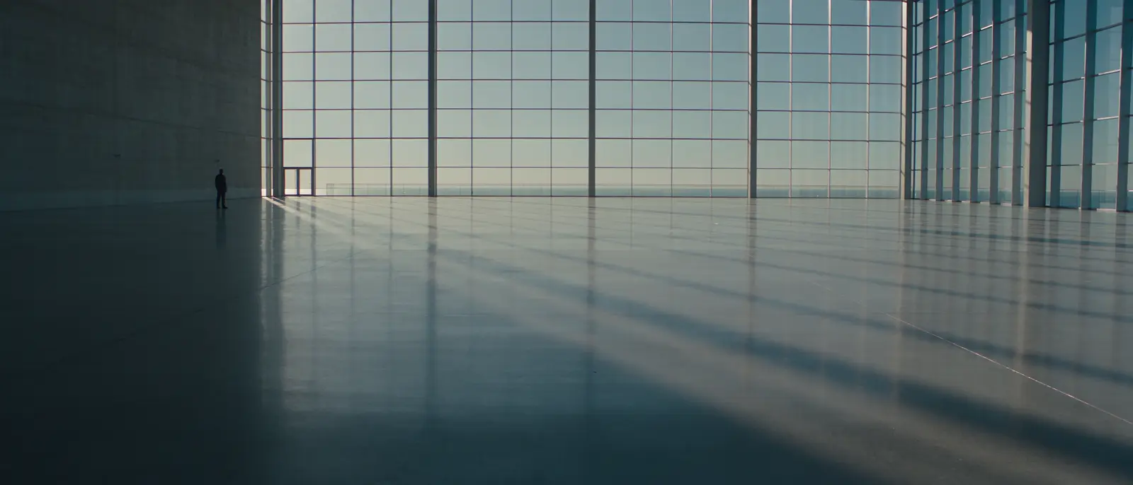 A tiny figure crossing an enormous atrium of glass and concrete.